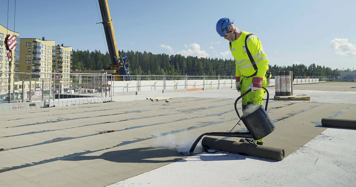 Katehuollon työntekijä asentaa kumibitumikermiä liikehuoneiston katolle.